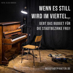 Hintergrund: Ein Klavier mit leerem Stuhl auf einer Bühne. Text: Wenn es still wird im Viertel... Gebt das Budget für die Stadtbezirke frei! Neustadtpiraten.de. Foto-Credit: Elisa Robock.